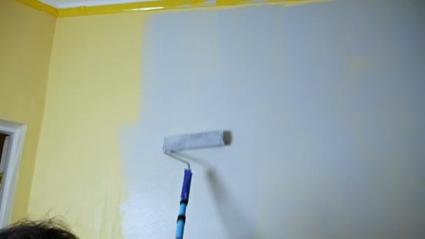Chica autodidacta alegre con un rodillo de construcción pinta una pared amarilla con pintura gris. Reparación de apartamentos independiente. Reparaciones frescas después de mudarse a un nuevo apartamento — Vídeo de stock