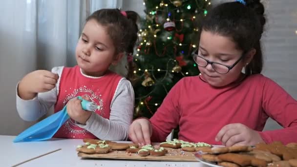 Barn gör julkakor. Barn inreder pepparkaksmannen, pepparkakor till julfirandet. Barn förbereder godis på bakgrunden av en julgran på en snöig vinterdag — Stockvideo