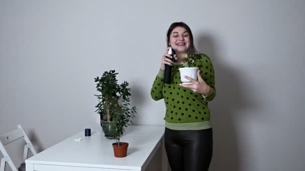 Uma senhora encantadora que cuida de plantas envasadas em casa, pulverizando água com uma pistola de pulverização sorrindo em casa. Pessoas e conceito de floricultura — Vídeo de Stock