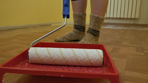 Chica empapa un rodillo de construcción en una sartén con pintura blanca. Auto reparación en la habitación — Vídeos de Stock