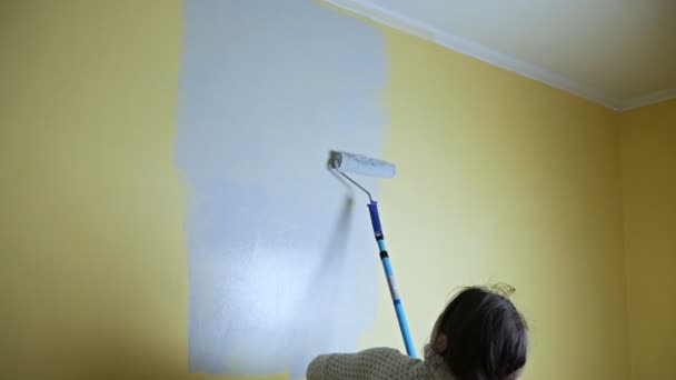 Радостная самоучка со строительным роликом красит желтую стену серой краской. Самостоятельный ремонт квартиры. Свежий ремонт после переезда в новую квартиру — стоковое видео