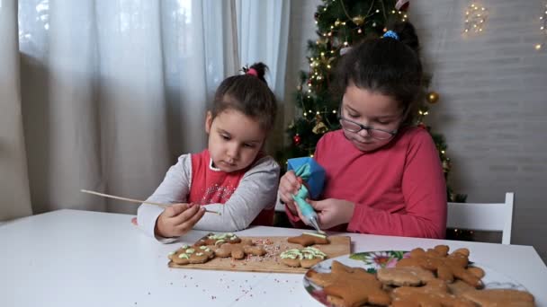 Τα παιδιά ψήνουν χριστουγεννιάτικα μπισκότα στο σπίτι.Η διαδικασία διακόσμησης χριστουγεννιάτικων μπισκότων. Τα παιδιά διακοσμούν τα μπισκότα μελόψωμου με τη μορφή χριστουγεννιάτικου δέντρου και μικρών ανθρώπων — Αρχείο Βίντεο