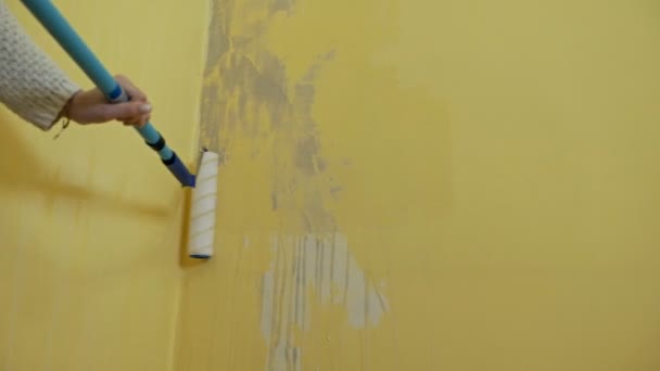 Ένα αυτοδίδακτο κορίτσι προετοιμάζει έναν τοίχο για τη ζωγραφική με έναν οδοστρωτήρα. Ένα κορίτσι εργάζεται επεξεργάζεται ένα κίτρινο τοίχο με ένα ρολό κατασκευής πριν από τη ζωγραφική. — Αρχείο Βίντεο