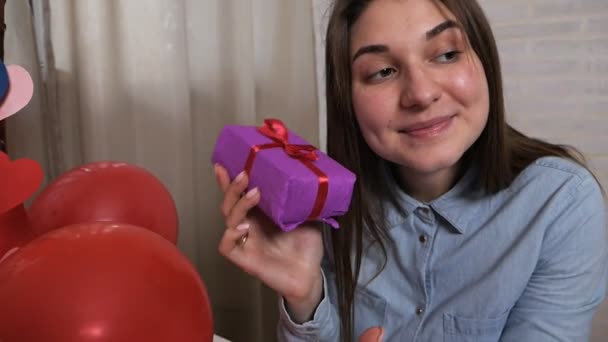 Una mujer sonriente sostiene una caja de regalo y agrada, piensa que hay. Concepto Valentine — Vídeo de stock