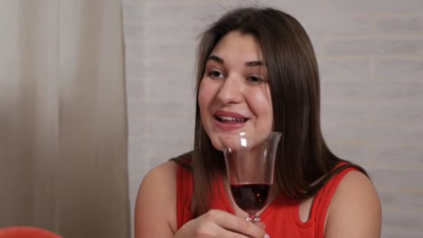 Uma menina bonita em um vestido vermelho na mesa bebe vinho de um copo e carrega chocolate, se comunica com seu marido. Dia dos namorados romântico — Vídeo de Stock