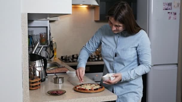 Handen van een jong meisje bestrooi pizza met geraspte kaas. Vrouw bereidt pizza voor haar geliefde man — Stockvideo