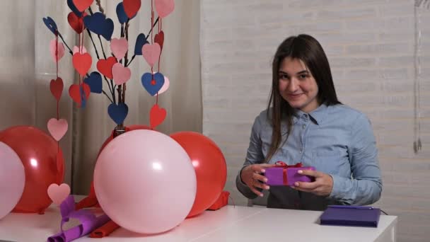 Una mujer sonriente sostiene una caja de regalo y agrada, piensa que hay. Concepto Valentine — Vídeos de Stock