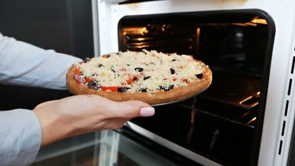 Een vrouw stopt pizza in de oven. Italiaanse pizza koken in een elektrische convectieoven. pizza met mozzarella kaas met salami tomaten — Stockvideo