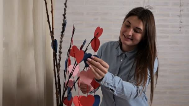 The girl is preparing decorations in the house for Valentines Day, a tree of hearts. Love, holiday — Stock Video