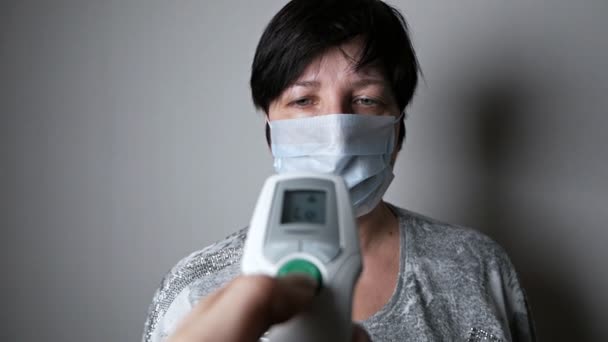 Появление симптомов коронавируса. Женщина измеряет температуру электронным термометром. Распространение китайского вируса Covid-19 . — стоковое видео