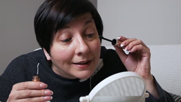 Frau malt Wimpern und blickt in den Spiegel, schwarze Wimperntusche im Hausflur Nahaufnahme — Stockvideo