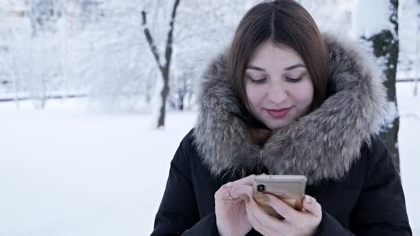 Een vrouw spreekt aan de telefoon op een koude winterdag. besneeuwde winter — Stockvideo