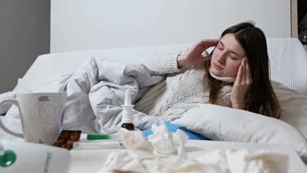 A mulher está doente na cama. A senhora está deitada na cama com comprimidos. Menina adulta doente. Tratamento de medicina em casa. Gripe e resfriados são sazonais. Uma mulher doente no quarto. Medicamentos na cama. Dor de cabeça — Vídeo de Stock