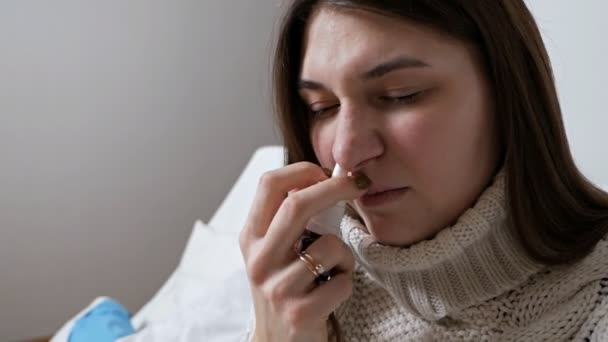 Portret van een aantrekkelijke brunette met griep. Het meisje heeft een verkoudheid, koorts, nek gewikkeld in warmte. Ze graaft haar neus met neusdruppels. — Stockvideo
