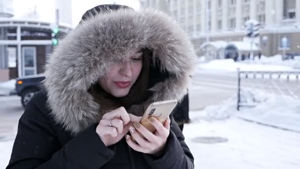 Mujer sosteniendo un teléfono en sus manos, tratando de llamar a un taxi en un frío día de invierno — Vídeos de Stock