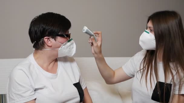 Madre e hija enmascaradas en casa comprobando la temperatura. Control de salud para Covid-19, Síntomas del Coronavirus, Control de Enfermedades — Vídeos de Stock