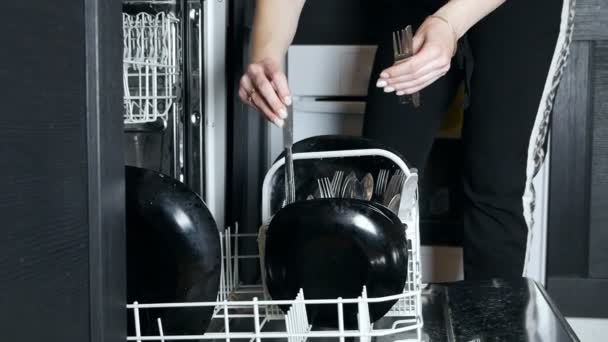 Carregando a máquina de lavar louça para colocar pratos e utensílios de cozinha no cesto, mãos de perto. Lavando pratos na cozinha, tarefas. Deveres domésticos usando eletrodomésticos modernos. câmera lenta — Vídeo de Stock