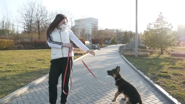 Een vrouw met een medisch masker op haar gezicht loopt door de straat met een Duitse herder. Coronovirus loop.Slow motion — Stockvideo