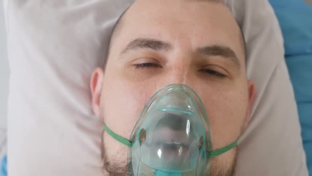 Молодий привабливий чоловік з кисневою маскою виглядає сумно і стурбований в лікарняному ліжку в клініці з хворобою Коронірус — стокове відео
