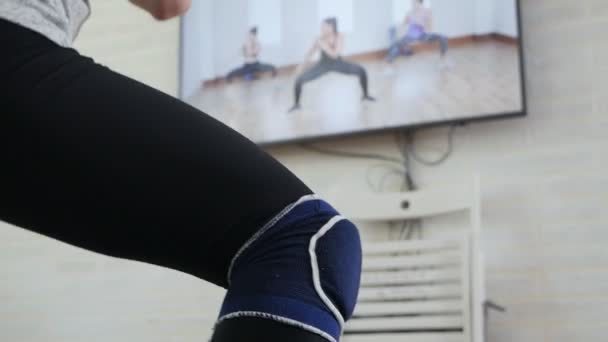 A girl does exercises while watching a program on TV at home — Stock Video