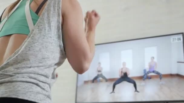 Ein Mädchen macht Übungen, während es zu Hause ein Programm im Fernsehen anschaut — Stockvideo