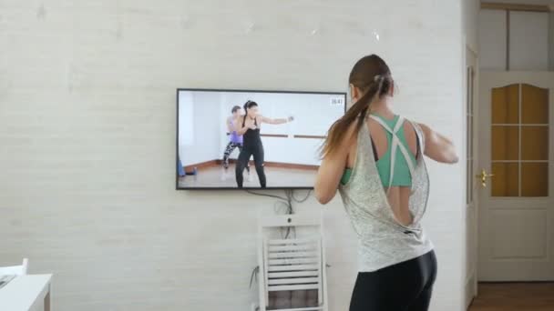 Fille sportive forte dans un haut et leggings saute vigoureusement et fait un exercice. Fille faisant des exercices de puissance dans une chambre spacieuse et lumineuse avec un intérieur blanc minimaliste — Video