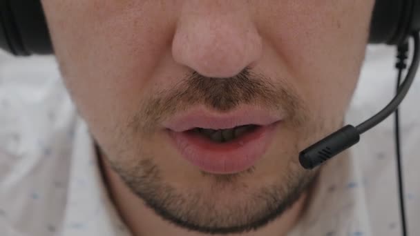 Primo piano di un uomo in cuffia che parla in un microfono, un operatore di call center che lavora, consulta un cliente online, uno studente che studia una lingua su Internet, ascolta una lezione — Video Stock