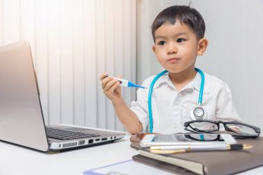 Doktor oynayan ve bir termometre tutan genç Asyalı çocuk.