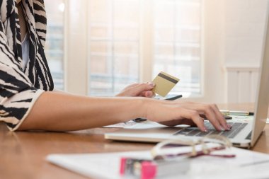 Kredi kartı tutan ve çevrimiçi alışveriş için dizüstü bilgisayar kullanarak bir işkadını