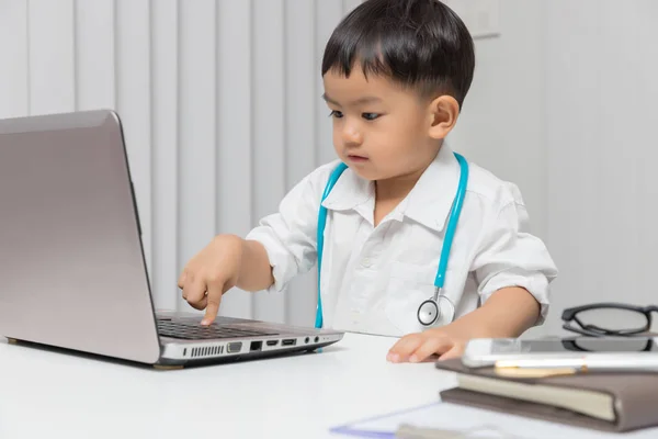 Young asian boy playing doctor and using computer laptop.