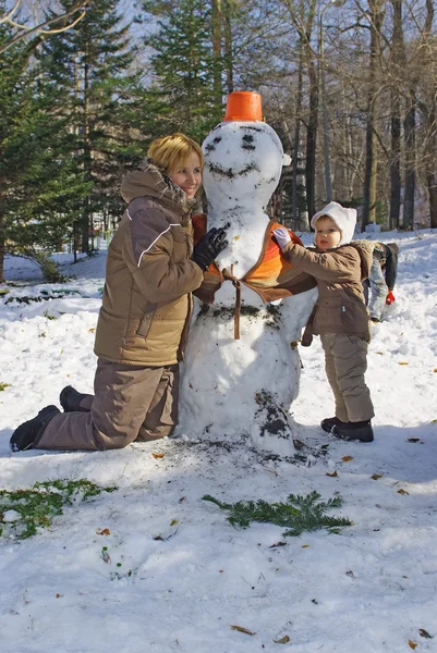 Glückliche Familie von Mutter mit Kind macht Schneemann im Schnee Outdoor-Hintergrund — Stockfoto