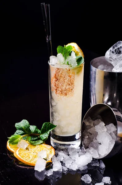 Koktajl alkoholowy - żółty napój pomarańczowy z plasterkiem cytryny, Zielona mięta w szklance z kostki lodu w shakerze na czarnym tle restauracja. Alkohol bar, miejsce. — Zdjęcie stockowe