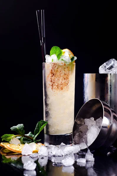 Cocktail alcolico - Orange drink giallo con fetta di limone, menta verde in un bicchiere con cubetto di ghiaccio in shaker su un ristorante di sfondo nero. Barra dell'alcool, spazio di copia . — Foto Stock