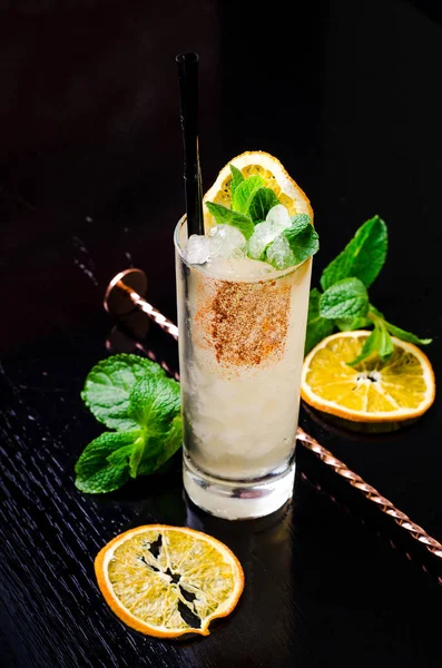 Alcoholic Cocktail - Yellow Orange drink with slice lemon, green mint in a glass with cube ice in shaker on a black background restaurant. Alcohol bar, copy space.