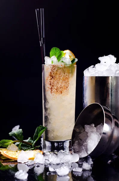 Alcoholic Cocktail: bebida de naranja amarilla con limón en rodajas, menta verde en un vaso con hielo de cubo en una coctelera en un restaurante de fondo negro. Alcohol bar, espacio de copia . Fotos De Stock