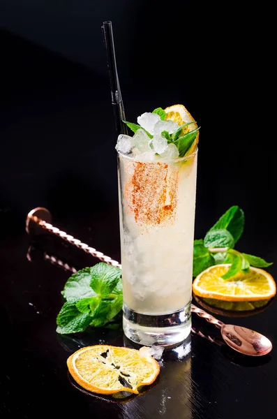 Cocktail alcolico - Orange drink giallo con fetta di limone, menta verde in un bicchiere con cubetto di ghiaccio in shaker su un ristorante di sfondo nero. Barra dell'alcool, spazio di copia . Immagine Stock