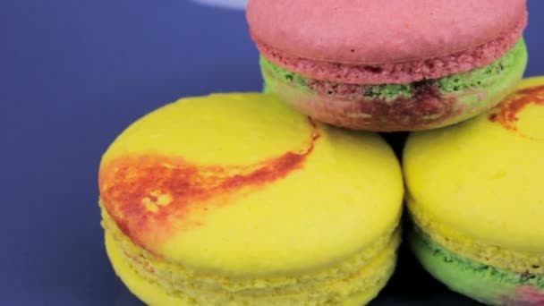 Pink, yellow and green macaroon quickly rotate on a blue plate, close-up — Stock Video