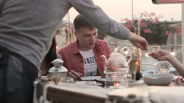 Офіціант прибирає святковий стіл біля трьох друзів — стокове відео