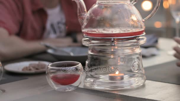 Прозрачный чайник с подогревом свечи в кафе, люди за столом — стоковое видео