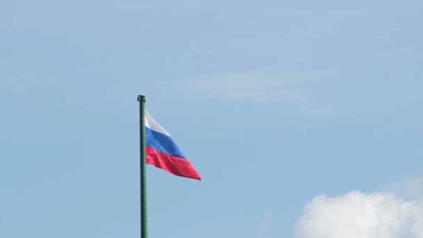 Bandera rusa ondea en el viento en el asta de la bandera en el fondo del cielo azul, El avión vuela entre las nubes — Vídeos de Stock