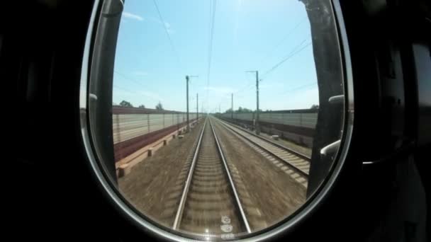 Трейн уходит со станции на зеленую равнину, движение по рельсам, вид с поезда — стоковое видео