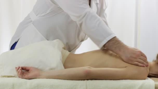 Массажист в массажном салоне для массажа спины молодой девушки — стоковое видео