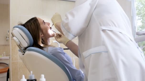 Врач, дантист проверяет зубы молодой пациентки — стоковое видео