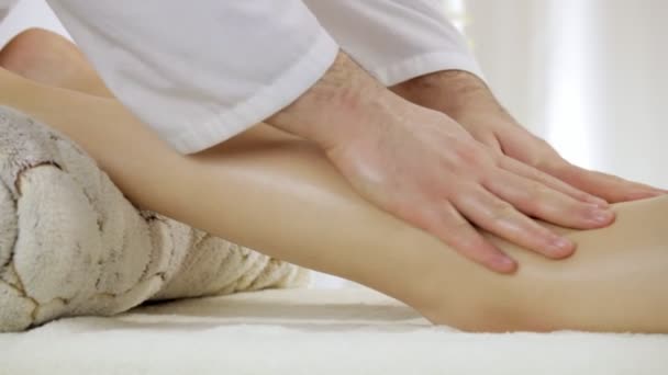 Доктор-массажист делает массаж ног для молодой девушки, снимает напряжение с мышц голени, кастрюлю — стоковое видео