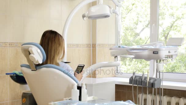 Studio dentista, la ragazza sulla sedia con il telefono e si gira sorridendo alla telecamera — Video Stock