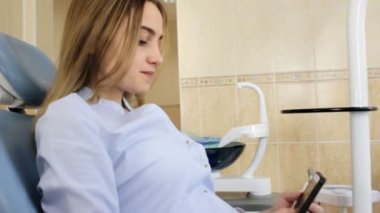 Diş hekimleri sandalyede oturan kız bir akıllı telefon kullanır