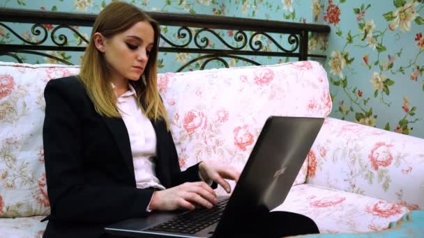 La empresaria se sienta en el sofá y escribe el texto en el portátil — Vídeos de Stock