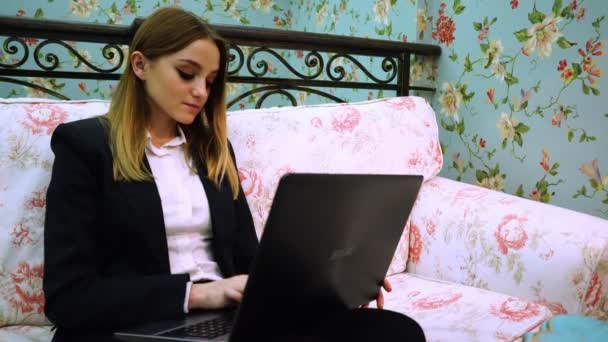 Uma jovem senhora de negócios senta-se em um sofá confortável e trabalha com um laptop — Vídeo de Stock