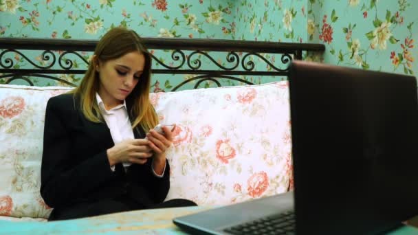 Bir dizüstü bilgisayar önünde bir smartphone cep telefonu ile tipik kız — Stok video