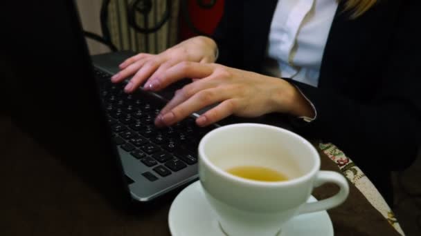Жінки руки друкувати текст на клавіатури ноутбука з чашку зеленого чаю — стокове відео